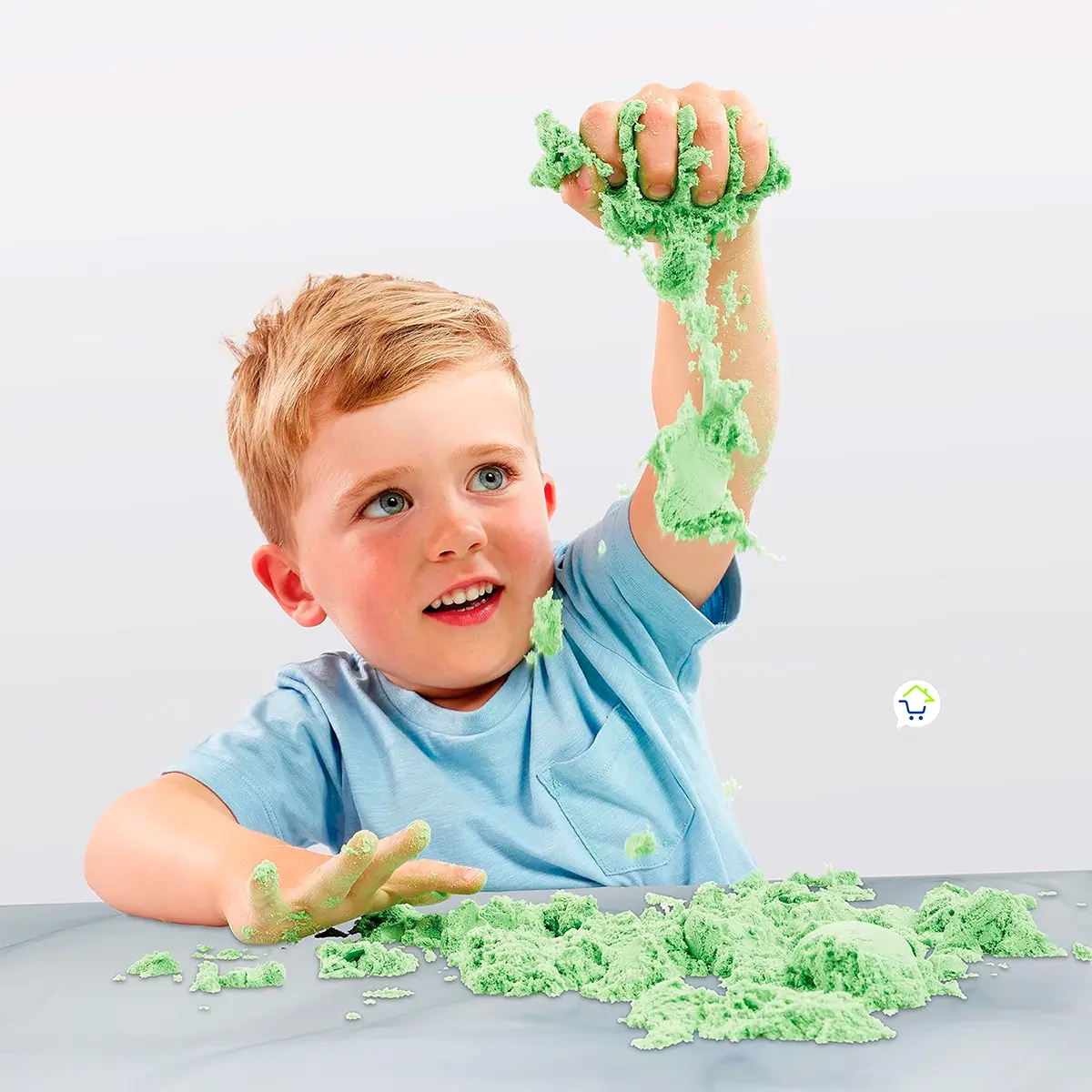 Niño jugando con arena mágica verde sobre una mesa.