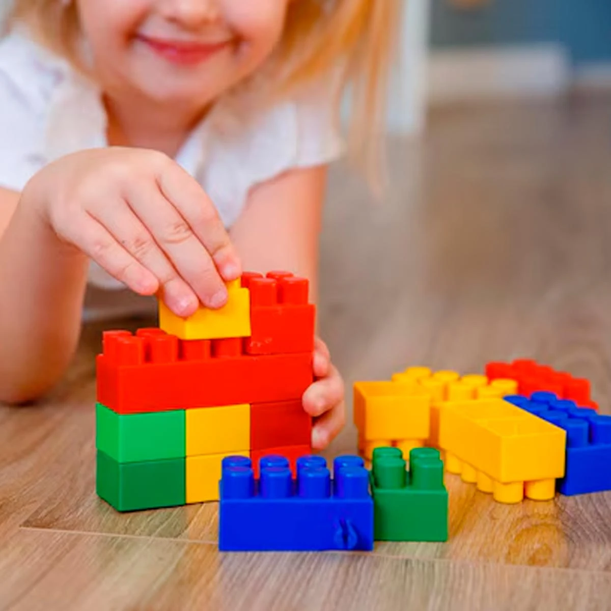 Niña jugando con bloques de construcción de colores en el suelo.