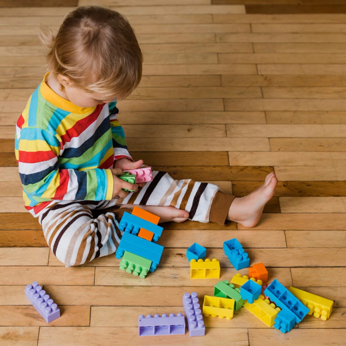 Niño jugando con bloques de construcción de colores en el suelo de madera.