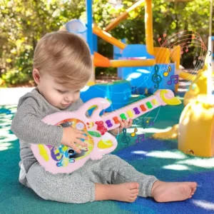 Niño pequeño jugando con una guitarra de juguete rosa en el parque.