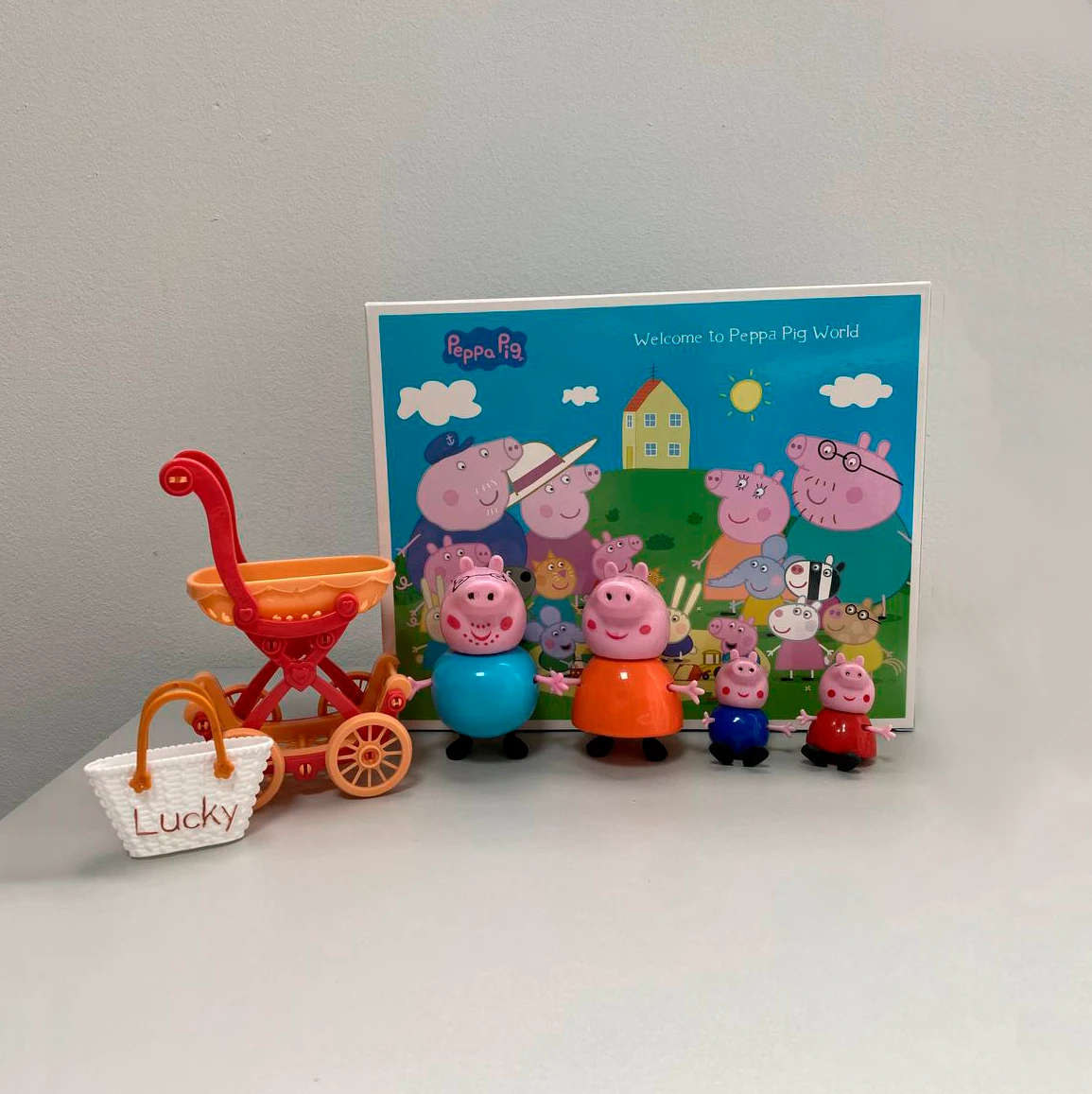 Figuras de Peppa Pig y su familia con cochecito y fondo colorido.